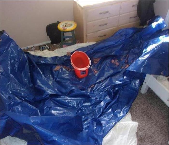 Bedroom with leaking ceiling into a bucket on a tarp